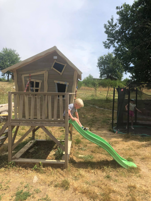 A child plays on a green slide by a crooked playhouse at Bell tent 6M, Campsite Junora in France.