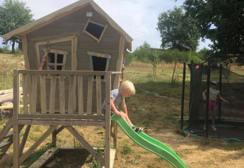 Un enfant joue sur un toboggan vert près d’une cabane penchée au Bell tent 6M, Camping Junora, France.