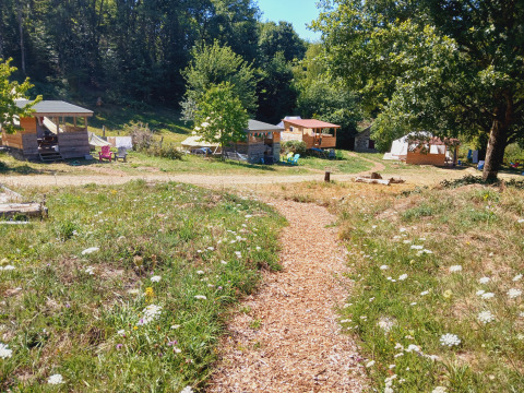 Pathway lined with wildflowers leads to Bell tent 6M and cabins at Campsite Junora in rural France.