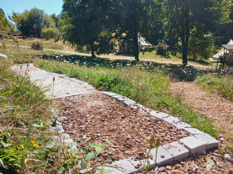 Wood chip and stone path leading to Bell tent “6M” at Campsite Junora, France, set in a green, wooded area.