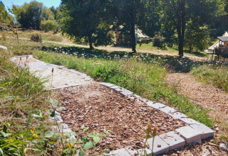 Wood chip and stone path leading to Bell tent “6M” at Campsite Junora, France, set in a green, wooded area.