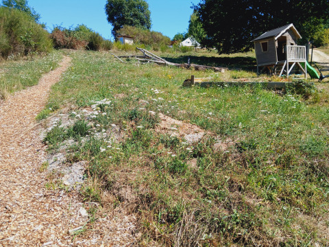 Woodchip path leads to a small wooden hut and grassy camp area at Bell tent 6M, Campsite Junora, France.
