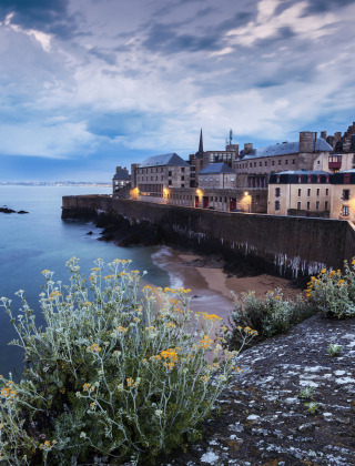 Vista de un pueblo costero histórico en Bretaña, Francia, con murallas y edificios antiguos junto al mar.