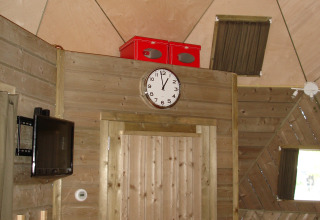 Vista interior de la tiny house Wooden Igloo en Holiday Park Delftse Hout, Países Bajos, con reloj y televisor.