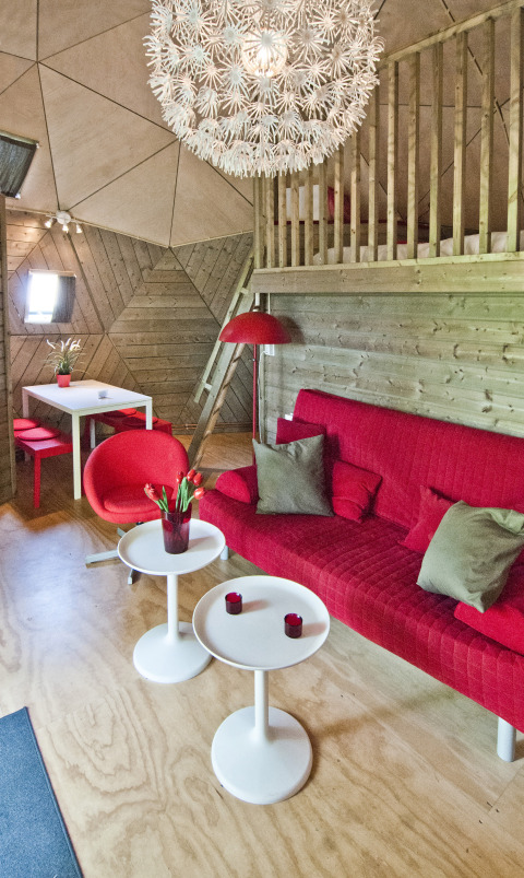 Soggiorno della tiny house Wooden Igloo al Holiday Park Delftse Hout, con divano rosso e lampada moderna.