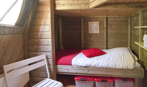 Cozy wooden bedroom with bed, red pillows, storage bins, and white chair in Wooden Igloo, Delftse Hout.