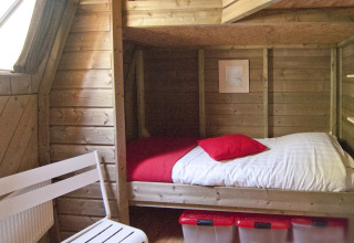 Holzverkleidetes Schlafzimmer mit Bett, roten Kissen und Stuhl in der Wooden Igloo im Delftse Hout Park.