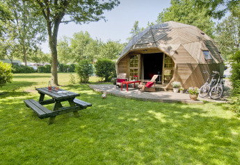 Casa tiny Wooden Igloo en Holiday Park Delftse Hout, Países Bajos, con bicicletas, banco y césped verde.