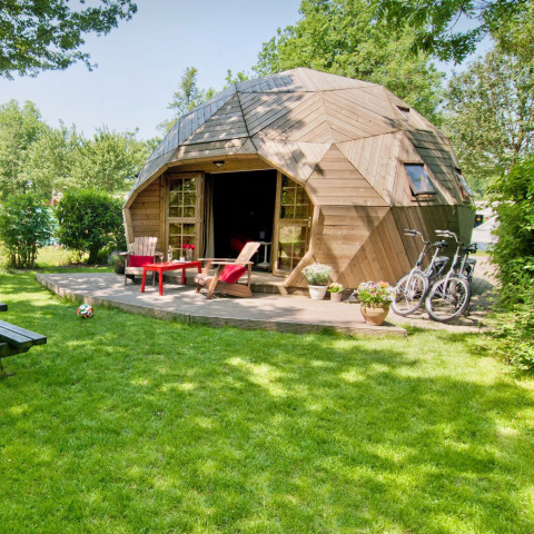 Træiglo-tiny house med terrasse og cykler i grøn have ved Holiday Park Delftse Hout, Holland.