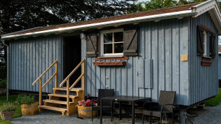 Tiny house with blue wood siding, staircase, and patio seating, captured on a grassy plot during daytime.