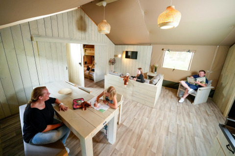 Interior photo of a safari tent with a family enjoying time together at the table and on the couch.
