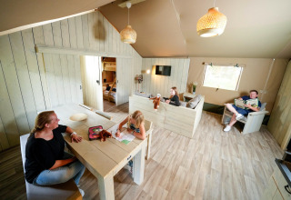 Interior photo of a safari tent with a family enjoying time together at the table and on the couch.