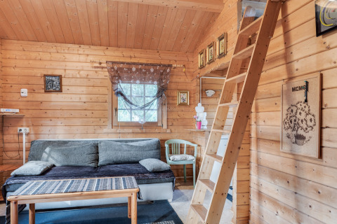 Lyst trækabineinteriør i Niederaula, Tyskland, med sofa, trappe til hems og dekorative billeder.