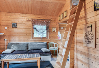 Lyst trækabineinteriør i Niederaula, Tyskland, med sofa, trappe til hems og dekorative billeder.