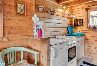 Cozy wooden cabin kitchen with a stove, coffee maker, fresh flowers in a vase, and utensils on the wall.