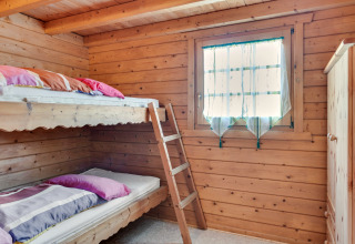 Cozy wooden cabin room with bunk beds, colorful pillows, curtained window, and wardrobe in Niederaula, Germany.