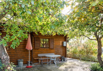 Træhytte ved navn Niederaula i Tyskland med grønne træer og terrassebord i solskin.