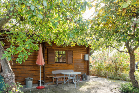 Træhytte ved navn Niederaula i Tyskland med grønne træer og terrassebord i solskin.