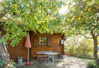 Træhytte ved navn Niederaula i Tyskland med grønne træer og terrassebord i solskin.