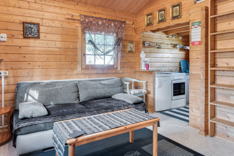 Hyggelig stue i træhytte 'Niederaula' i Tyskland med sofa, køkken og dekorerede vægge.