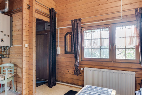 Indretning af en træhytte med store vinduer, gardiner, radiator og synlige rør i Niederaula, Tyskland.