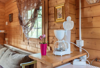 Hyggekrog i træhytte 'Niederaula' i Tyskland med kaffemaskine, blomst og sollys gennem vindue.