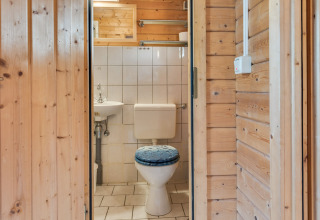 Et lille badeværelse i en træhytte ved Niederaula i Tyskland med toilet, håndvask og flisevægge.