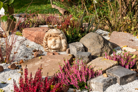 Rock garden with purple heather, child’s head sculpture, and stones at the Niederaula cabin in Germany.