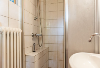 Lille brusekabine med hvide fliser, håndvask og radiator i kabinen Niederaula, Tyskland.
