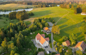 Foto aerea di una tiny house in Germania circondata da campi verdi, alberi e un lago vicino.