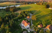 Photo aérienne d’une tiny house en Allemagne entourée de champs verts, d’arbres et d’un lac proche.