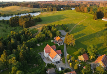 Photo aérienne d’une tiny house en Allemagne entourée de champs verts, d’arbres et d’un lac proche.