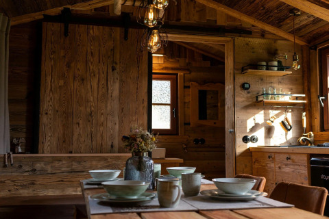 Interior de una tiny house en Alemania, mesa de comedor de madera y acogedora cocina rústica iluminada.