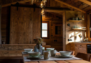 Interior de una tiny house en Alemania, mesa de comedor de madera y acogedora cocina rústica iluminada.