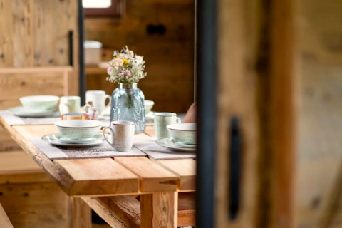 Table en bois dressée avec vaisselle en céramique et vase de fleurs dans un tiny house en Allemagne.
