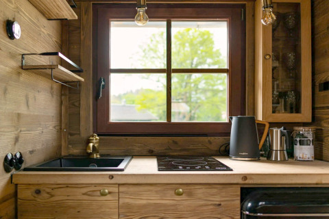 Petite cuisine dans un Tiny House avec meubles en bois, grande fenêtre, évier et bouilloire électrique.