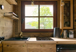 Petite cuisine dans un Tiny House avec meubles en bois, grande fenêtre, évier et bouilloire électrique.