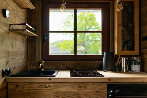 Acogedora cocina de Tiny House con paneles de madera, ventana grande, fregadero y hervidor eléctrico.
