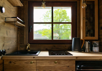 Petite cuisine dans un Tiny House avec meubles en bois, grande fenêtre, évier et bouilloire électrique.