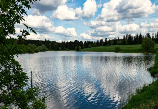 Vue paisible sur un lac reflétant les nuages, près de prairies verdoyantes et d'une Tiny House en Allemagne.