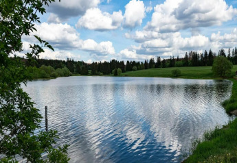 Vue paisible sur un lac reflétant les nuages, près de prairies verdoyantes et d'une Tiny House en Allemagne.