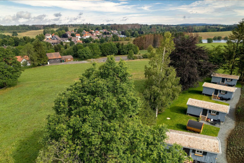 Vue aérienne d’un espace Tiny House en Allemagne avec des prés verts, des arbres et un village en fond.