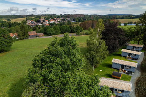 Vista aérea de un área de Tiny House en Alemania con campos verdes, árboles y un pueblo al fondo.