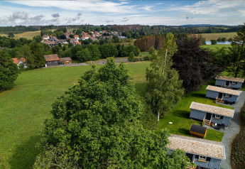 Vue aérienne d’un espace Tiny House en Allemagne avec des prés verts, des arbres et un village en fond.