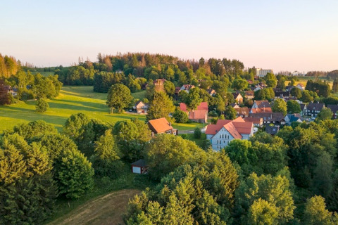 Village au coucher du soleil avec champs verts et Tiny House en Allemagne, entourée de nombreux arbres.