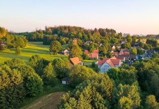 Village au coucher du soleil avec champs verts et Tiny House en Allemagne, entourée de nombreux arbres.