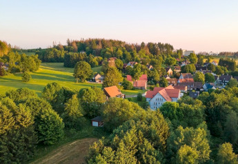 Villaggio al tramonto con campi verdi e Tiny House in Germania, immersa tra alberi rigogliosi.
