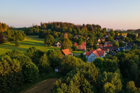Pueblo al atardecer con campos verdes y Tiny House en Alemania, rodeado de árboles frondosos y naturaleza.