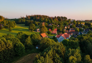 Pueblo al atardecer con campos verdes y Tiny House en Alemania, rodeado de árboles frondosos y naturaleza.