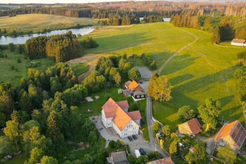 Vue aérienne d'une tiny house en Allemagne entourée de champs verts, d'arbres et d’un lac paisible à la campagne.